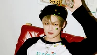 Chenle from NCT Dream playfully tossing colorful candies while seated in a cozy setting.