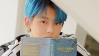 Yeonjun von Tomorrow X Together mit blauen Haaren, der ein Buch hält und eine traumhafte Ästhetik verkörpert.