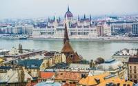 Ein Panoramablick auf das ungarische Parlamentsgebäude, das seine atemberaubende Architektur entlang der Donau zeigt, umrahmt von einer historischen Stadtsilhouette und Dächern.