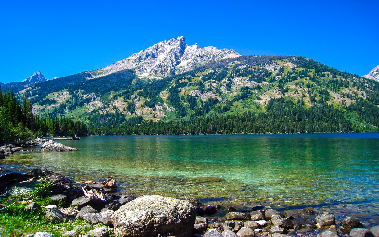 Une montagne éloignée avec un lac et des pierres au premier plan (lac émeraude, parc national de grand teton, wyoming, ciel bleu, eau claire)