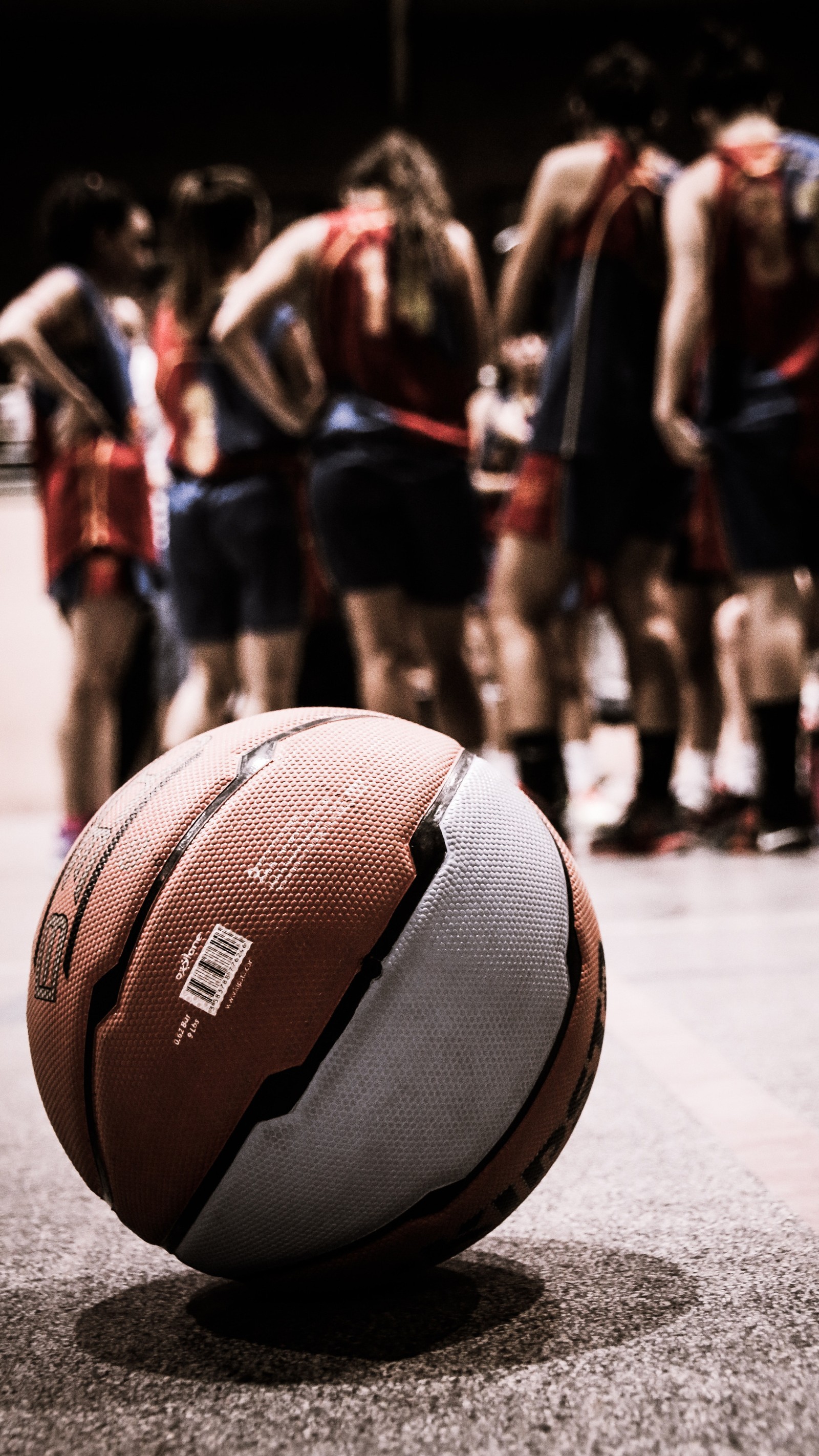 Basketball ball on the ground with a group of people in the background (basketball, nba, bball, zedgebball18, sports)