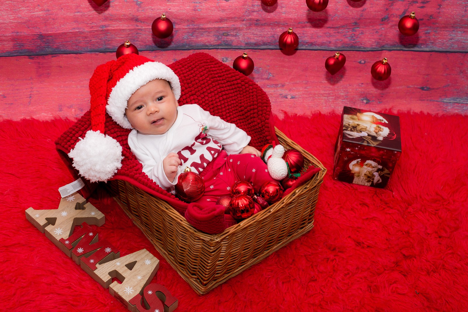 Bebé árabe con un gorro de papá noel sentado en una cesta con adornos (love bebe, feliz navidad)