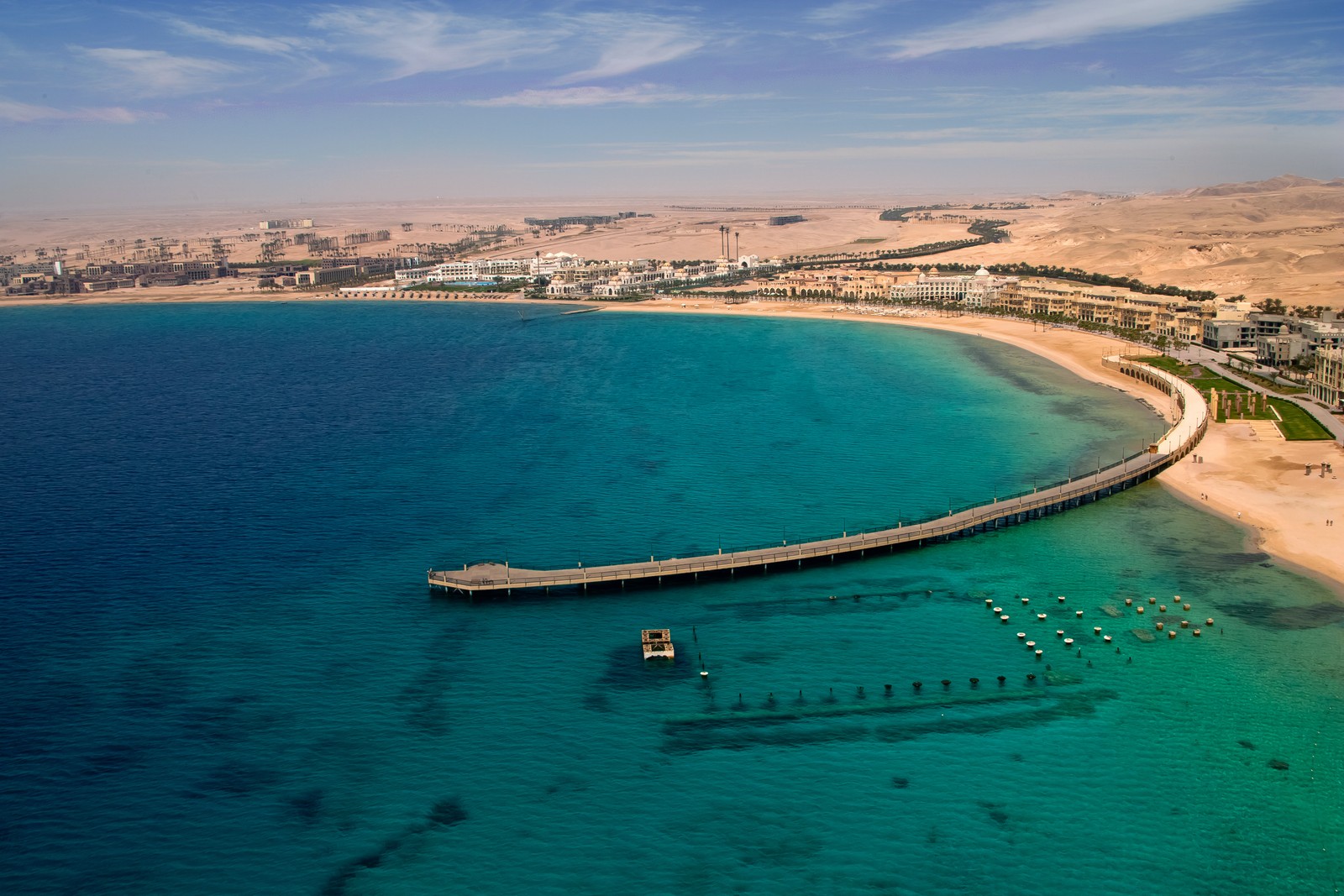 Vista em arco de um píer no meio do oceano com uma praia e um resort de praia (estância, água, recursos hídricos, mar, costa)