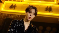 Johnny de NCT 127 dans une tenue en cuir frappante, sur un fond jaune vif avec des enseignes d'inspiration asiatique.