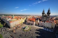 Uma vista panorâmica da histórica Praça da Cidade Velha de Praga, apresentando o icônico Relógio Astronômico e uma deslumbrante arquitetura medieval sob um céu azul claro.