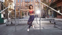 Selena Gomez pose avec confiance dans une tenue sportive contre un décor urbain, mettant en avant son style athlétique.