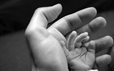 Un moment tendre de connexion entre la main d'un parent et les petits doigts d'un enfant en noir et blanc.