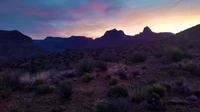 Dawn over the Arizona badlands, showcasing a vibrant sky and rugged mountain silhouettes in the Grand Canyon landscape.