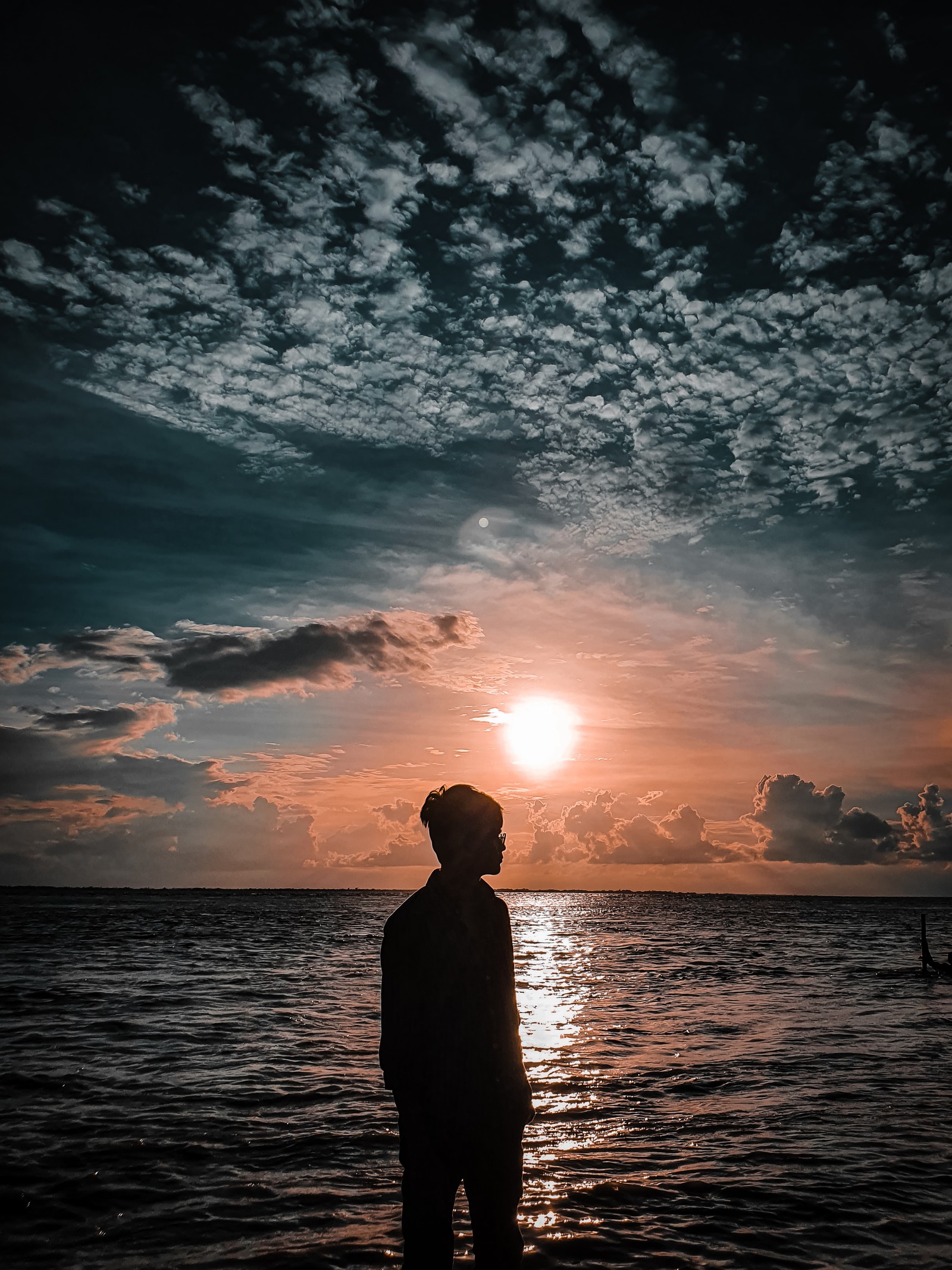 Un hombre de pie en la playa mirando el atardecer (solo, chico solitario, mejor, mejor foto, niño)