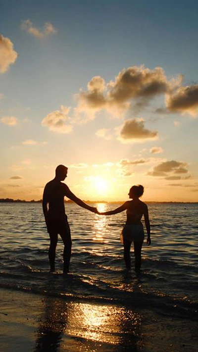 Pareja en silueta tomados de la mano al atardecer junto al océano