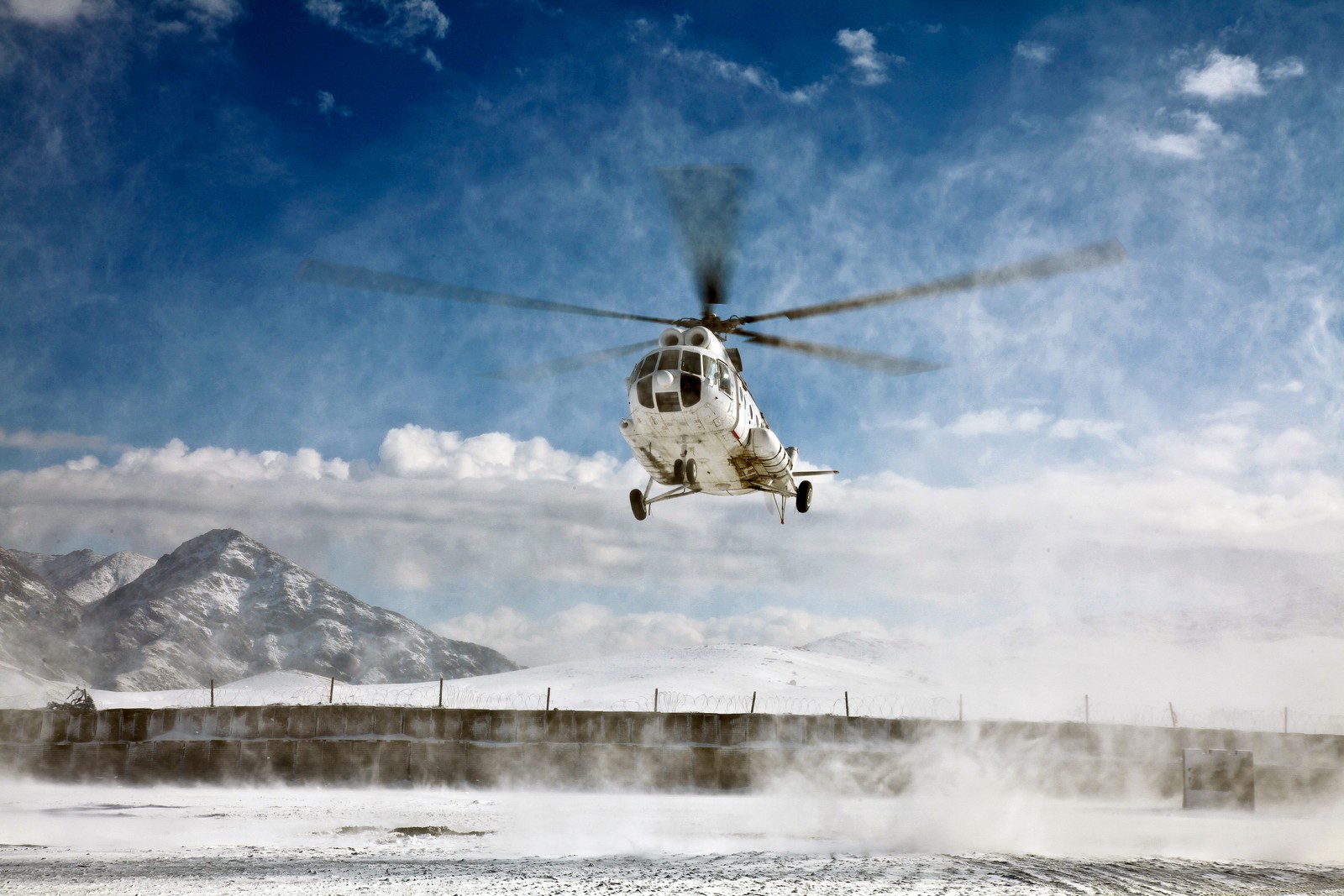 Um helicóptero voando sobre um campo nevado com uma montanha ao fundo (helicóptero, aeronave de rotor, rotor de helicóptero, aeronave, helicóptero militar)