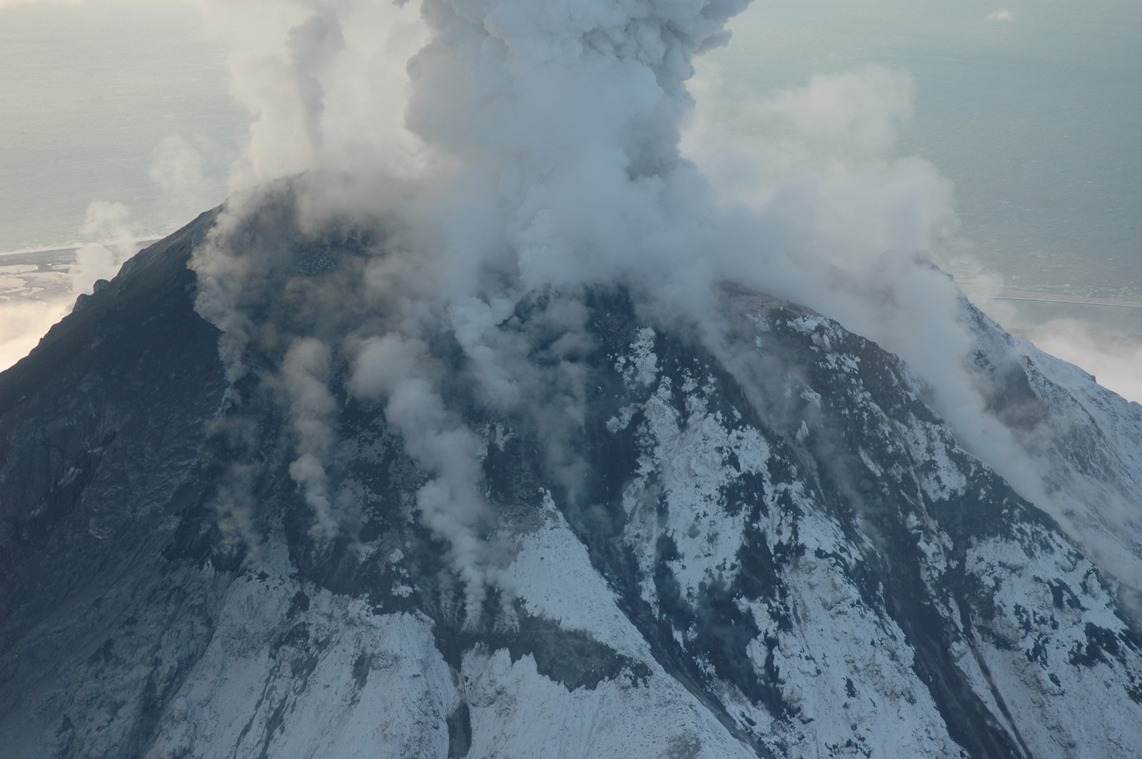 La fumée s'élève d'une montagne avec un avion qui passe (crête, stratovolcan, volcan, lave, volcan bouclier)