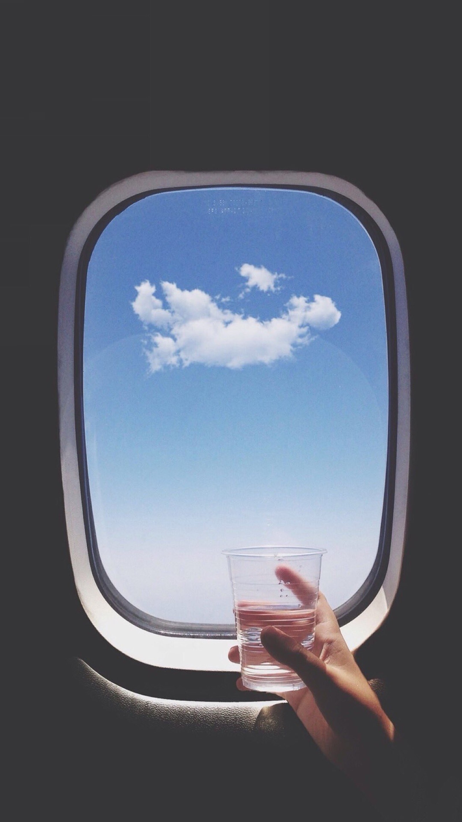 Someone holding a glass of water in front of a window (airplane, cloud, window)