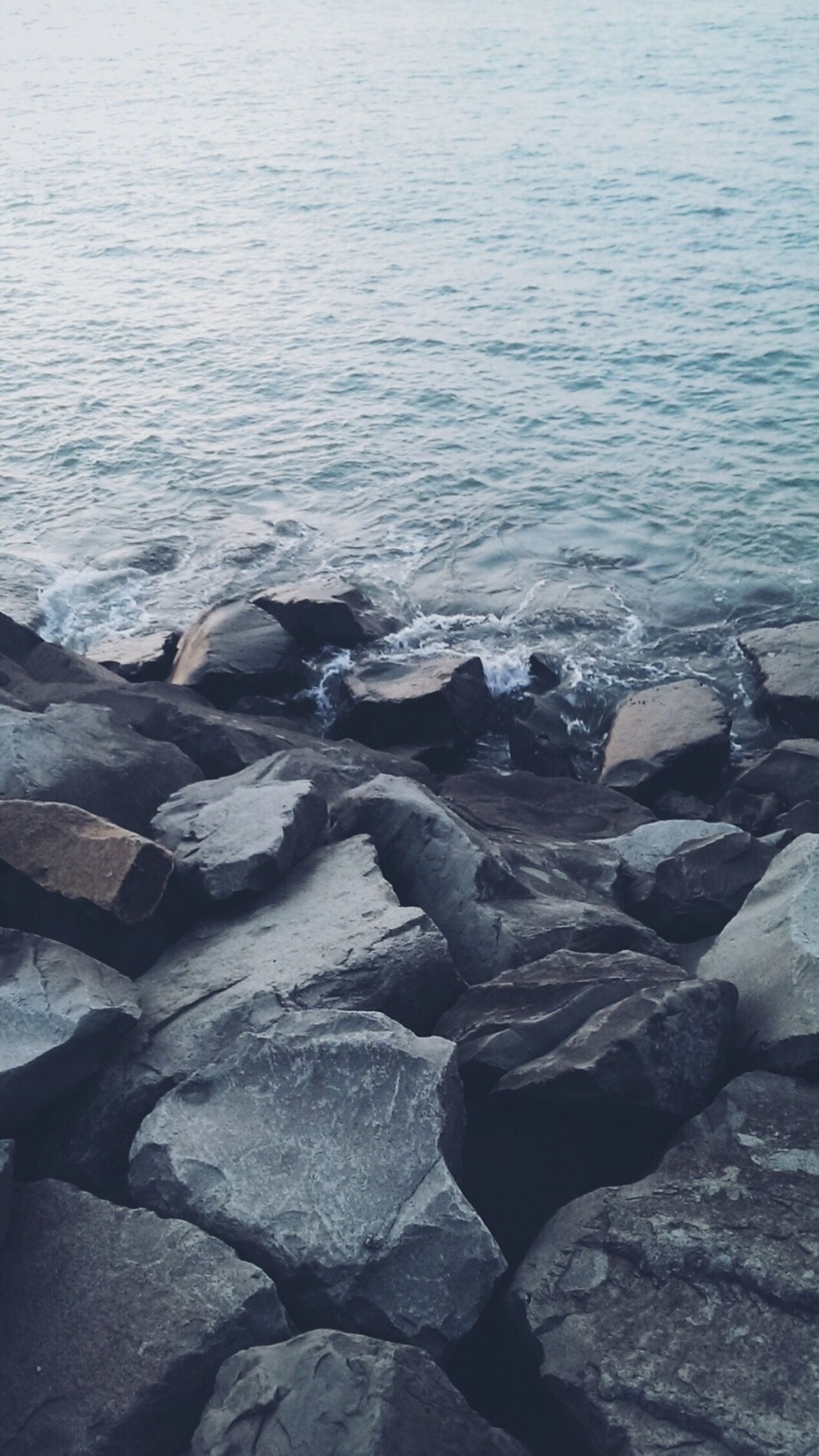 Há uma pessoa em pé sobre uma pedra ao lado da água (relaxamento, rochas, rocky, mar, costa)