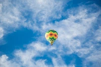 Colorido globo aerostático surcando un brillante cielo azul salpicado de nubes cúmulos esponjosas.