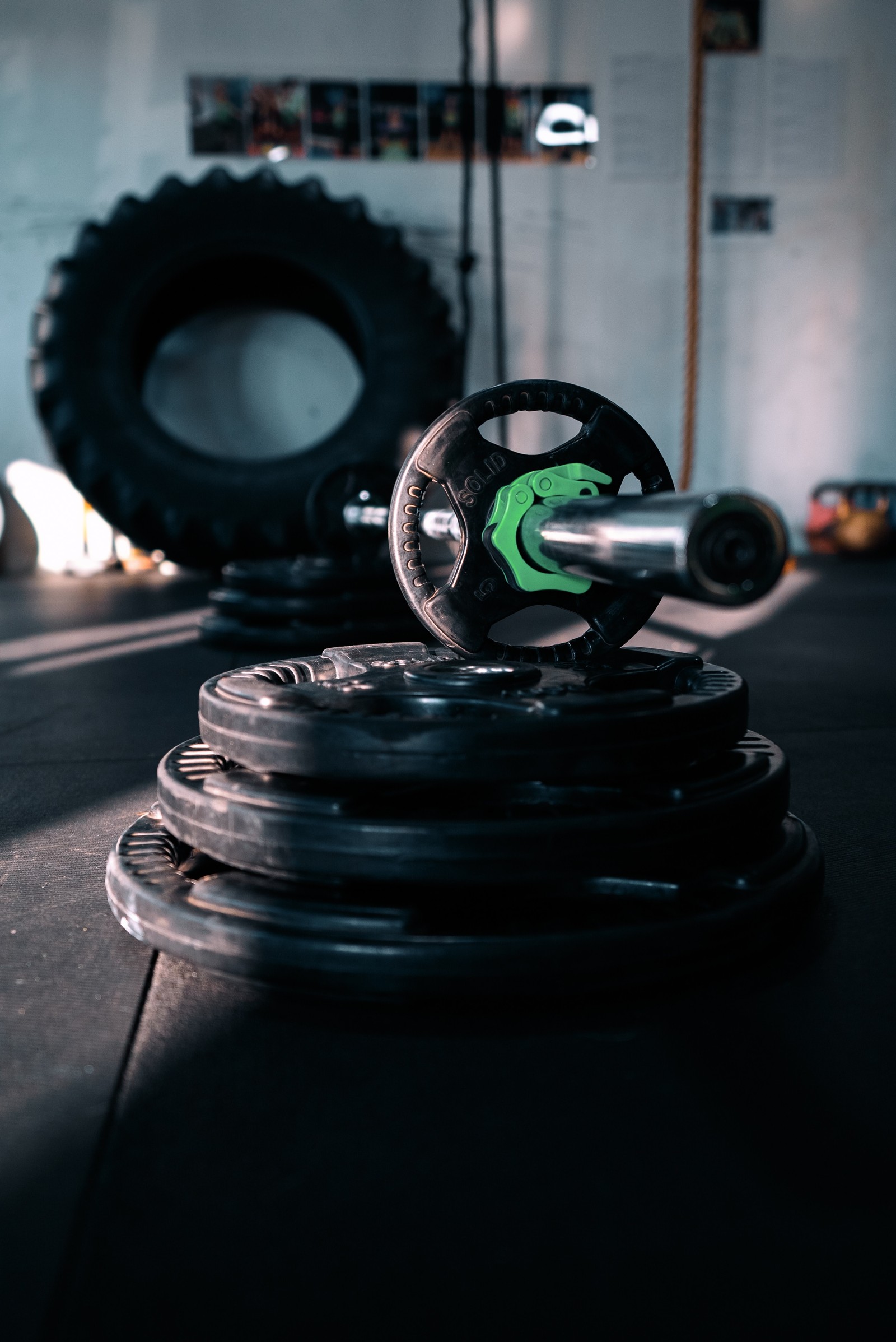 Hay una mancuerna negra y verde sobre un suelo negro (centro de fitness, entrenamiento de fuerza, ejercicio, crossfit, barra)