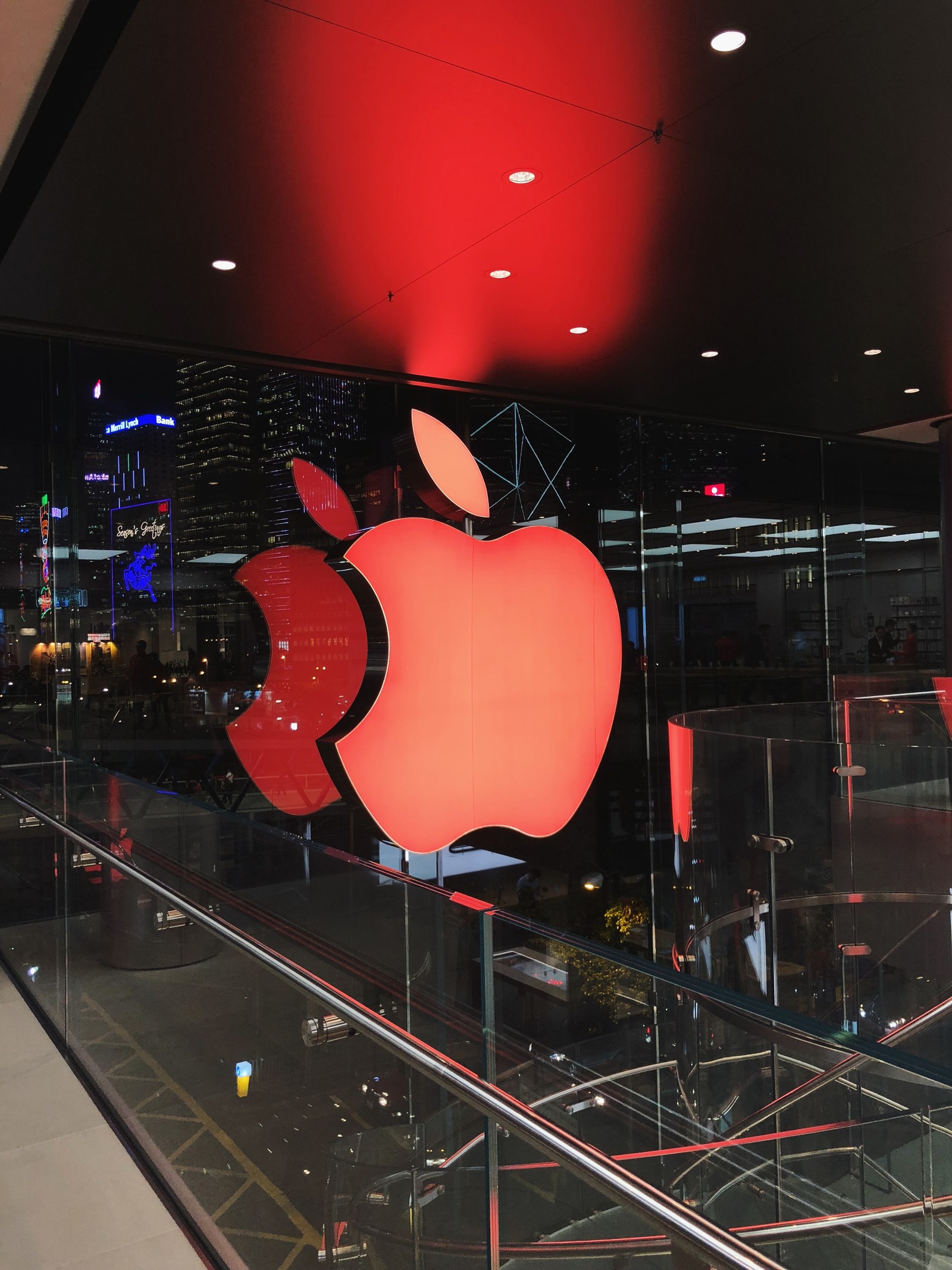 Hay una pared de vidrio con un logo de manzana roja sobre ella (manzana, iluminación, carmín, manzanas, fruta)