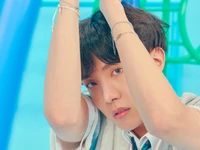 J Hope do BTS: Expressão cativante em um cenário azul vibrante