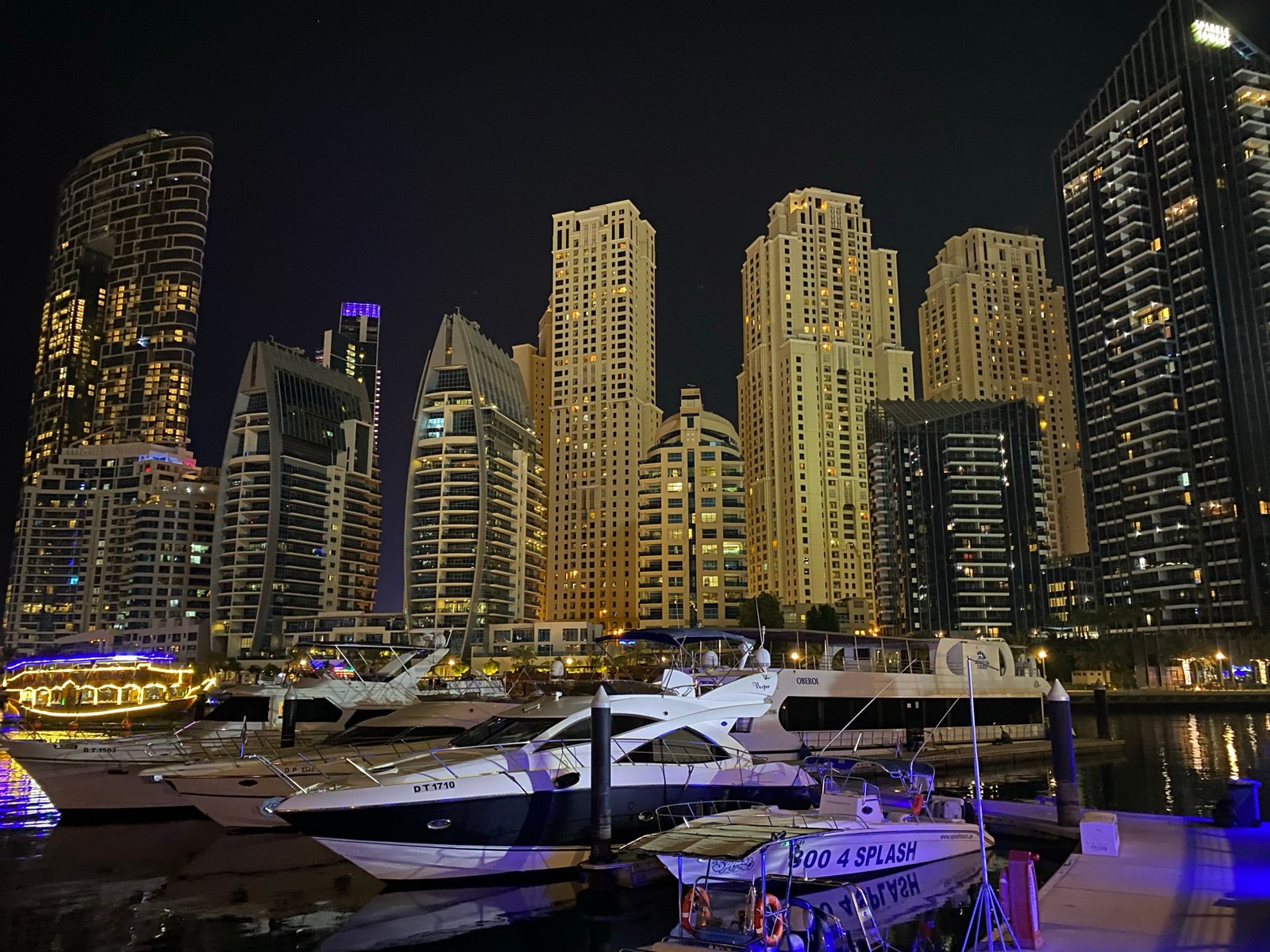 Barcos estão atracados em um porto com um horizonte urbano ao fundo (dubai, marina de dubai, paisagem urbana, arranha céus, noite)