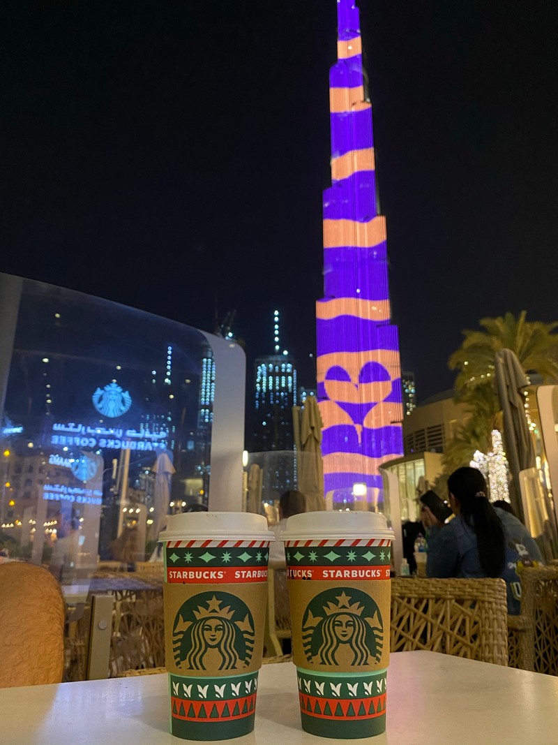 Стаканы starbucks стоят на столе перед высоким зданием. (дубай, dubai, burj khalifa, ночь, башня)