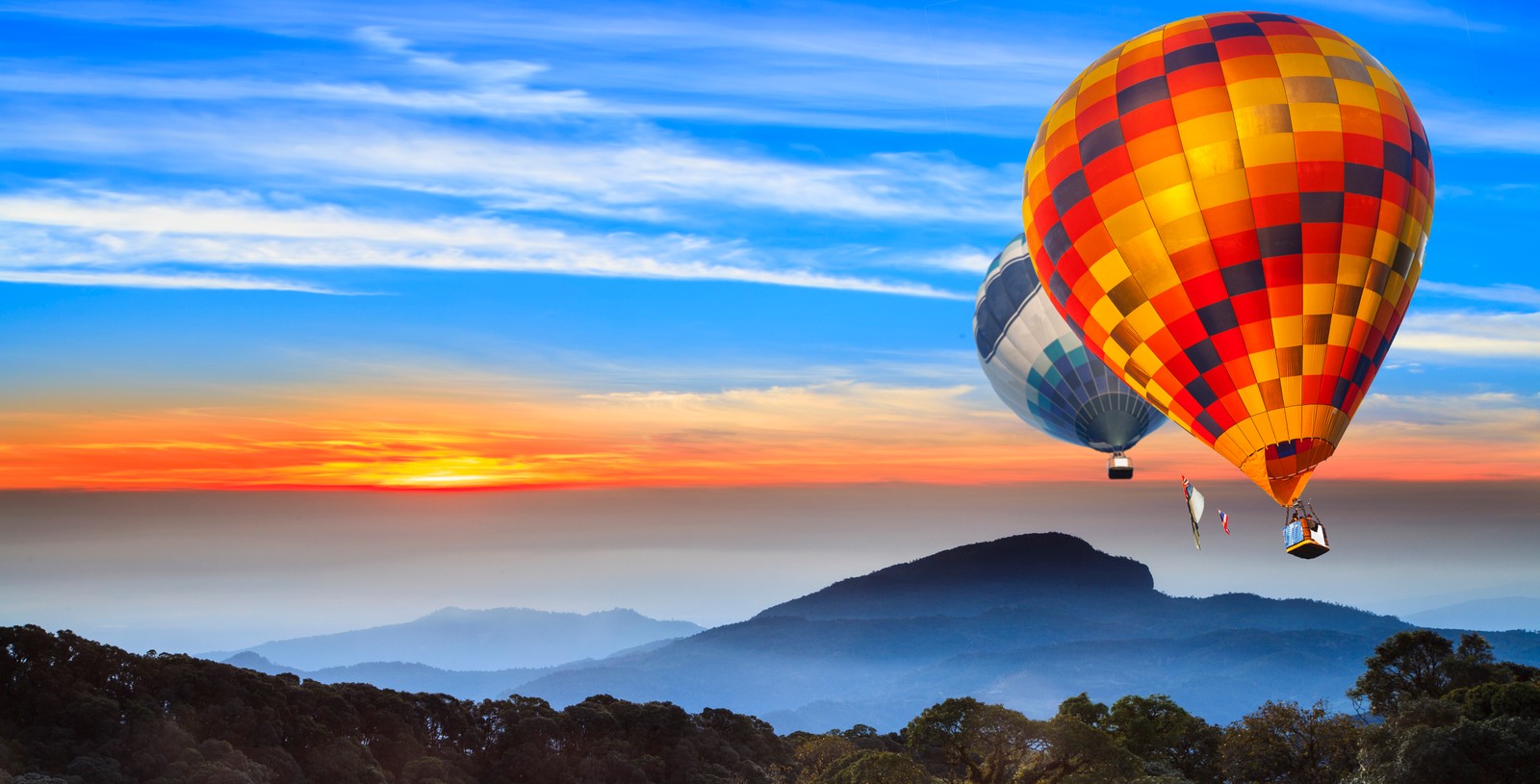 Une montgolfière volant au-dessus d'une montagne avec un coucher de soleil en arrière-plan (ballons à air chaud, paysage, collines, lever de soleil, matin)