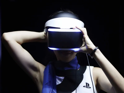 Pessoa usando um headset PlayStation VR, com as mãos levantadas atrás da cabeça, iluminada contra um fundo escuro.