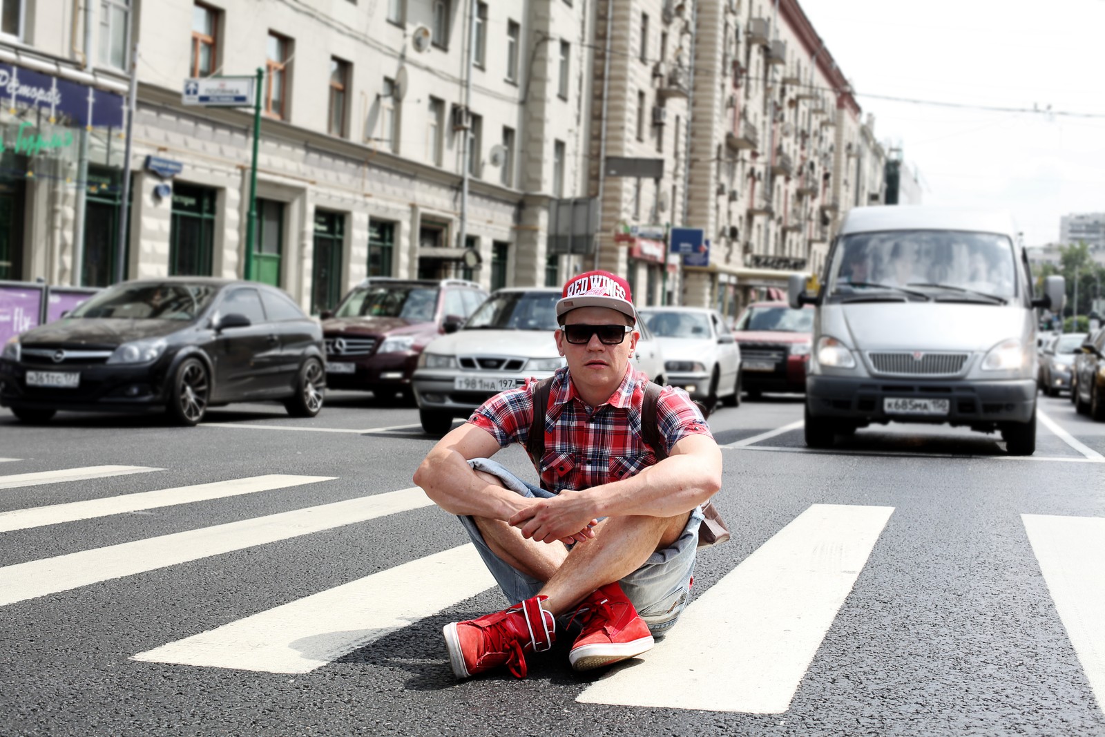 Un homme est assis par terre sur un skate (rue, voiture, transport, mode de rue, route)