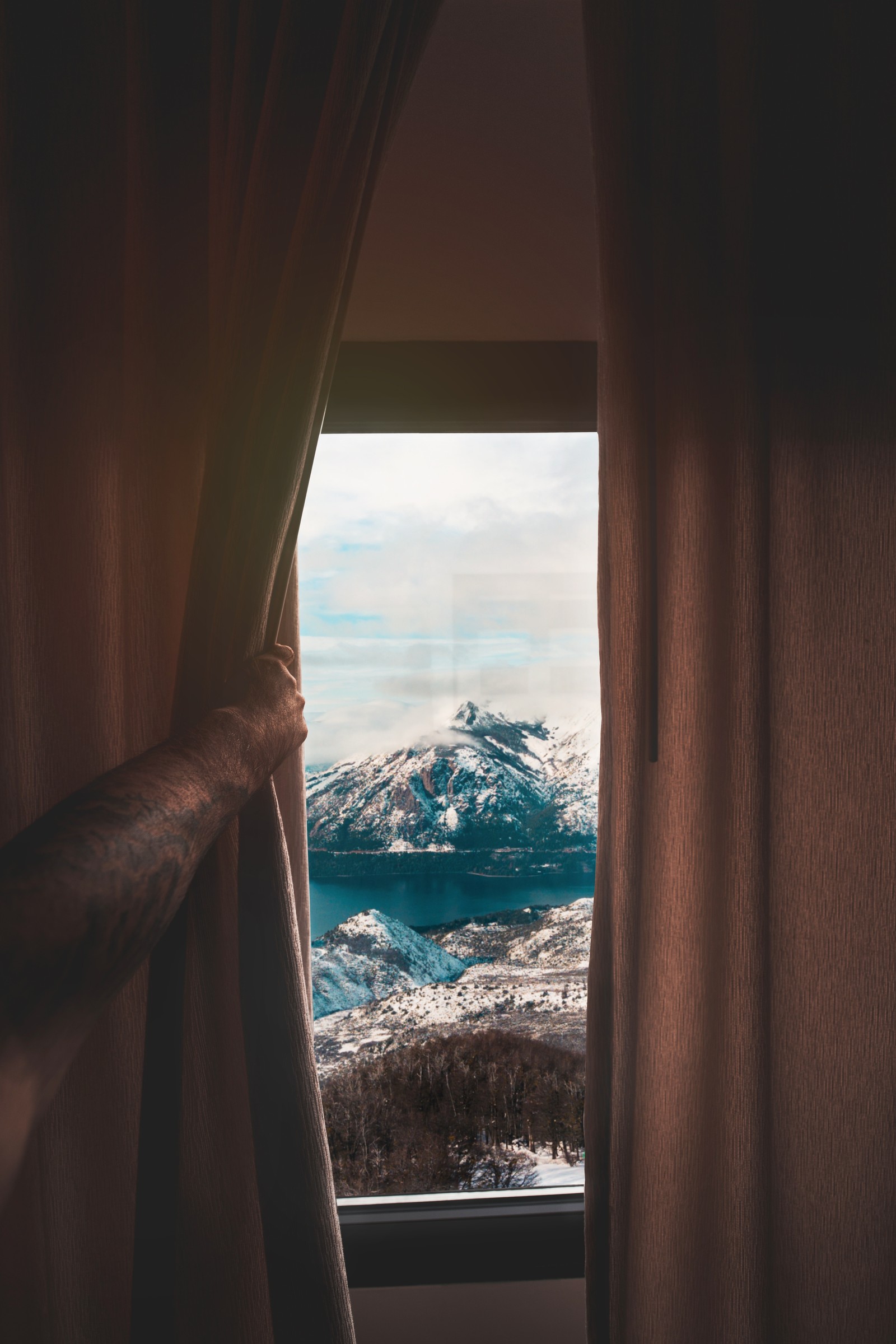 Arafed view of a mountain range from a window with curtains (window, curtain, room, tree, water)