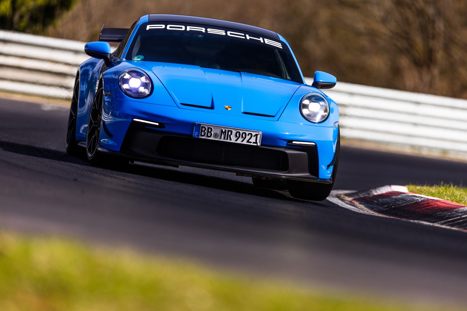 Luftaufnahme eines blauen sportwagens, der auf einer rennstrecke mit einem weißen zaun fährt (porsche 911 gt3, rennstrecke, 2022, manthey performance kit, 5k)