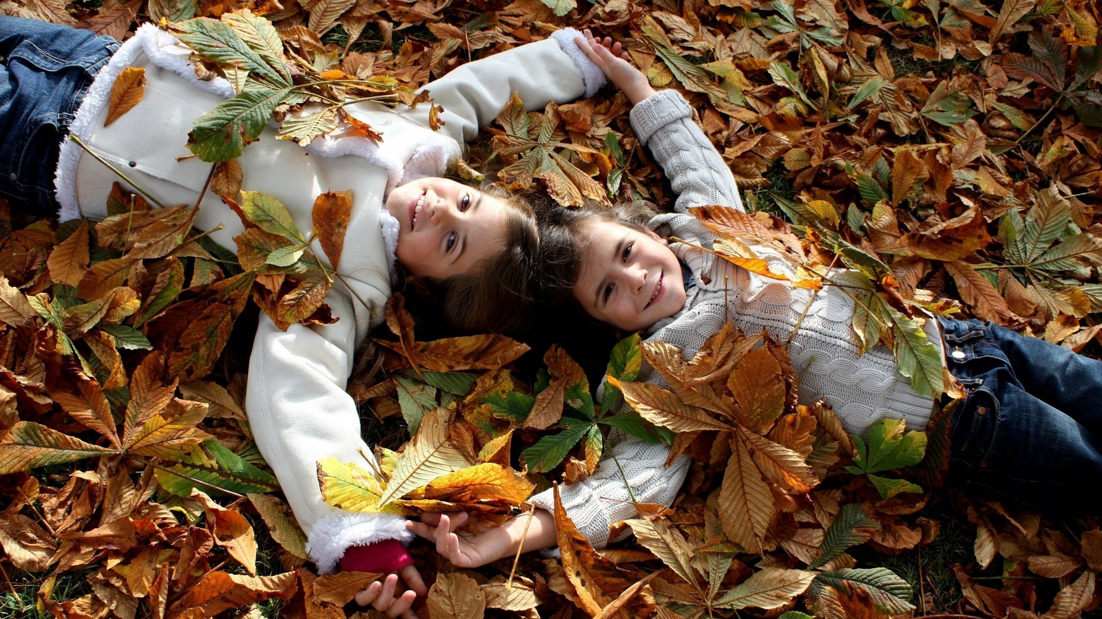 Deux enfants allongés sur le sol dans un tas de feuilles (automne, arbre, feuilles, amitié, enfant)