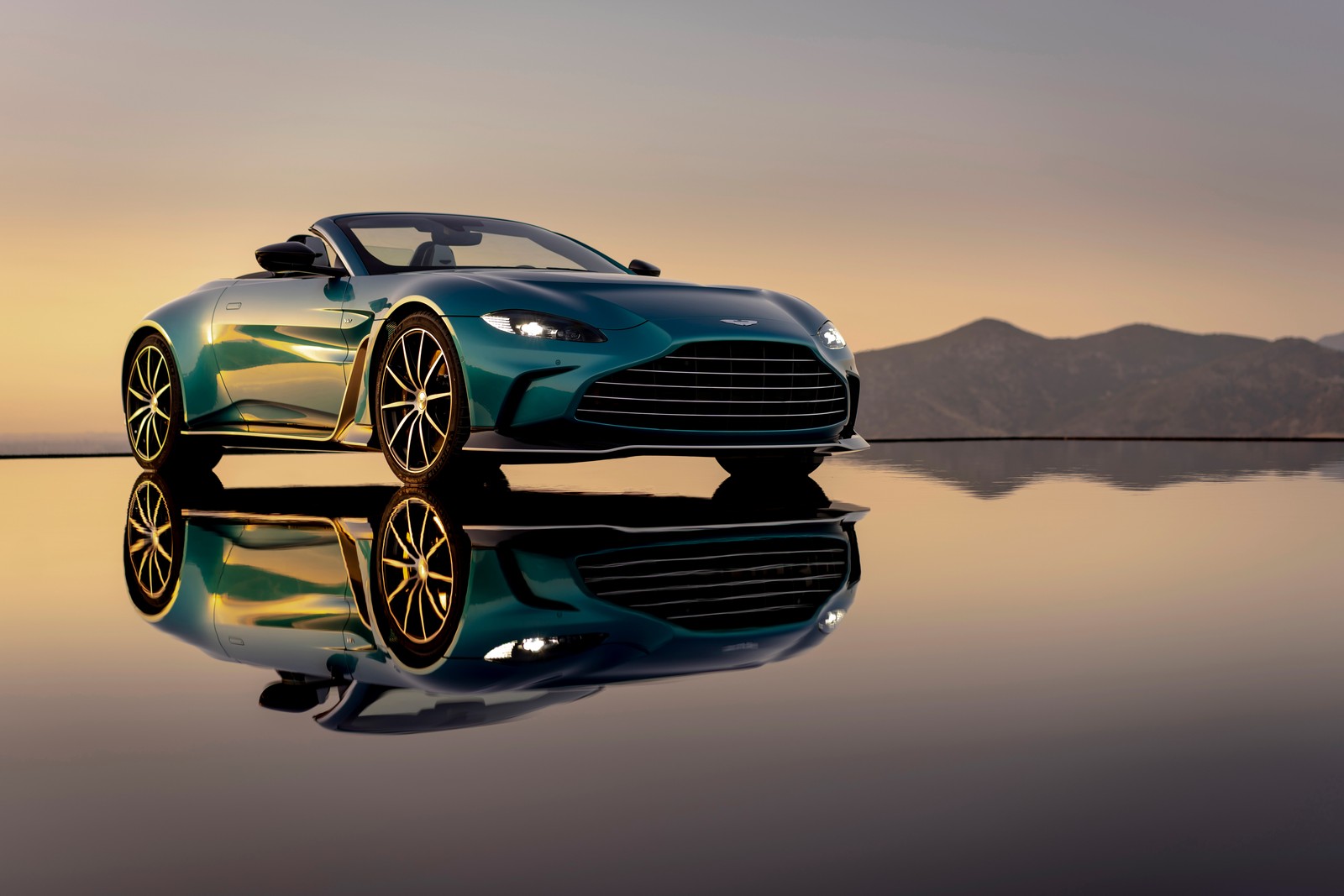 Un primer plano de un coche sobre una superficie reflectante con montañas al fondo (aston martin v12 vantage roadster, supercoches, 2022, 5k, 8k)