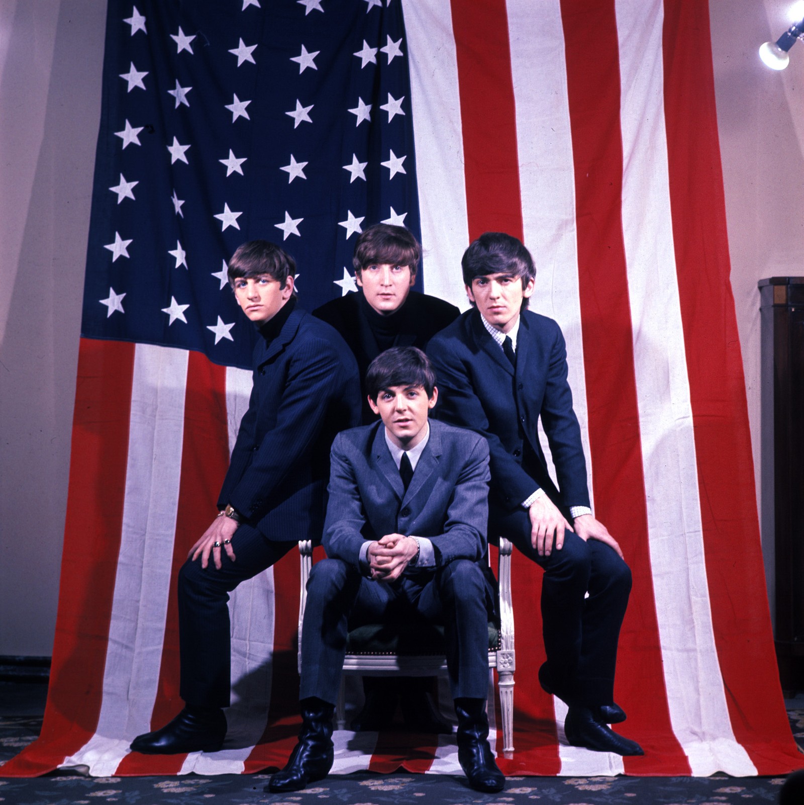 Uma foto de um grupo de homens de terno sentados em frente a uma bandeira americana (ringo starr, the beatles, evento, desempenho, diversão)