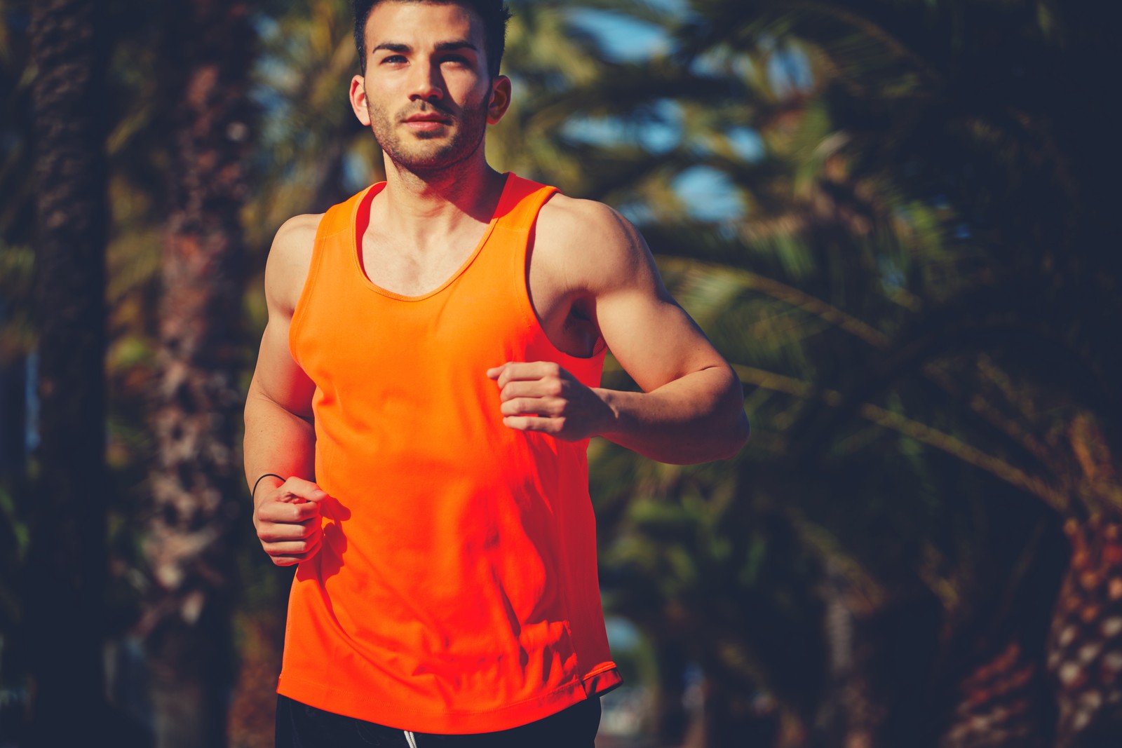 Homem árabe correndo com um colete laranja brilhante e shorts pretos (correndo, braço, recreação, músculo, atletismo)