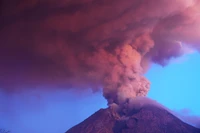 Plume éruptive s'élevant d'un volcan bouclier sous un ciel dramatique.