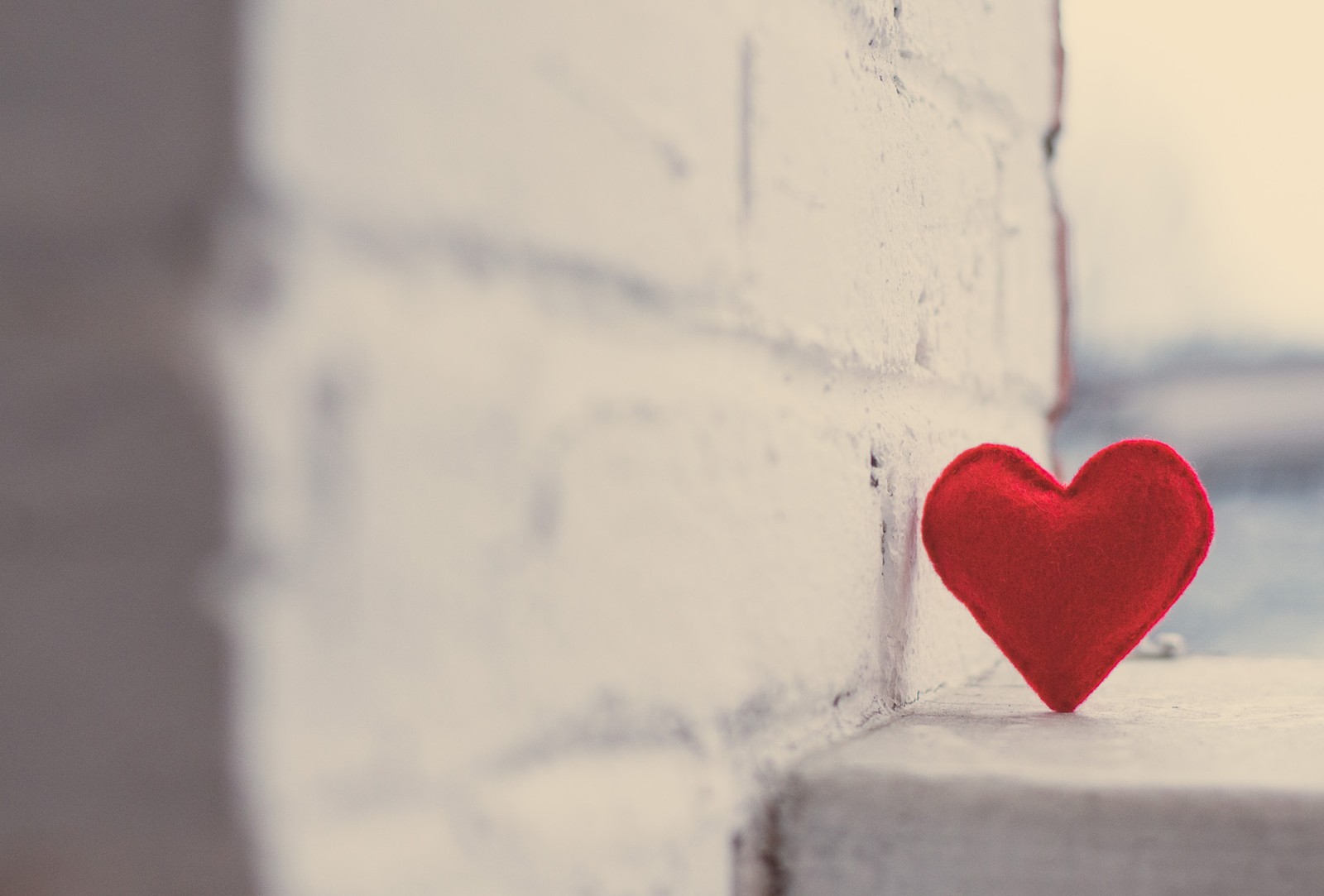 Il y a un cœur rouge posé sur une corniche près d'un mur en briques. (cœur, rouge, amour, arts créatifs, design)