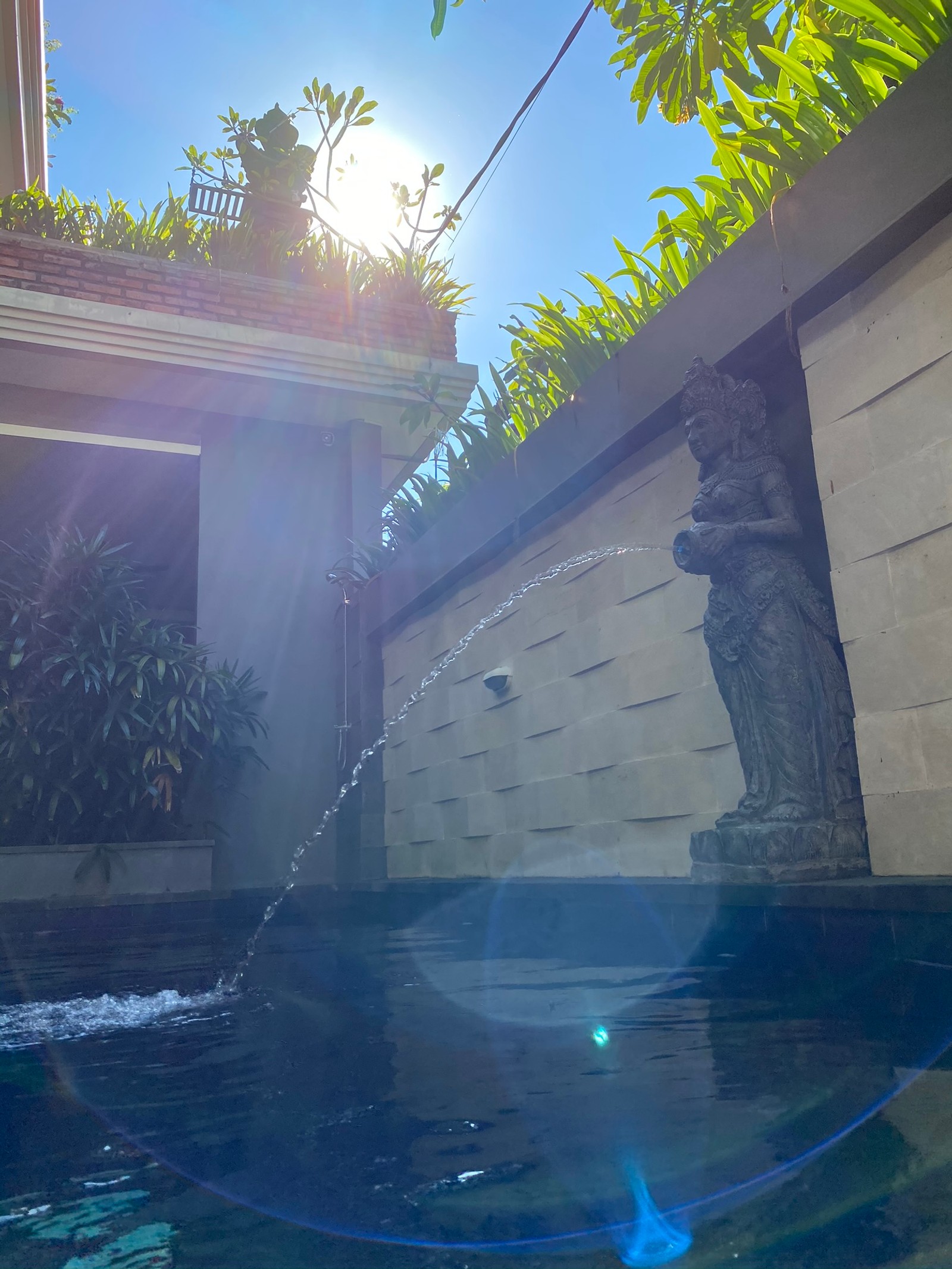 Há uma fonte no meio de uma piscina com o sol brilhando (bali, reflexo, piscina, água, recursos hídricos)