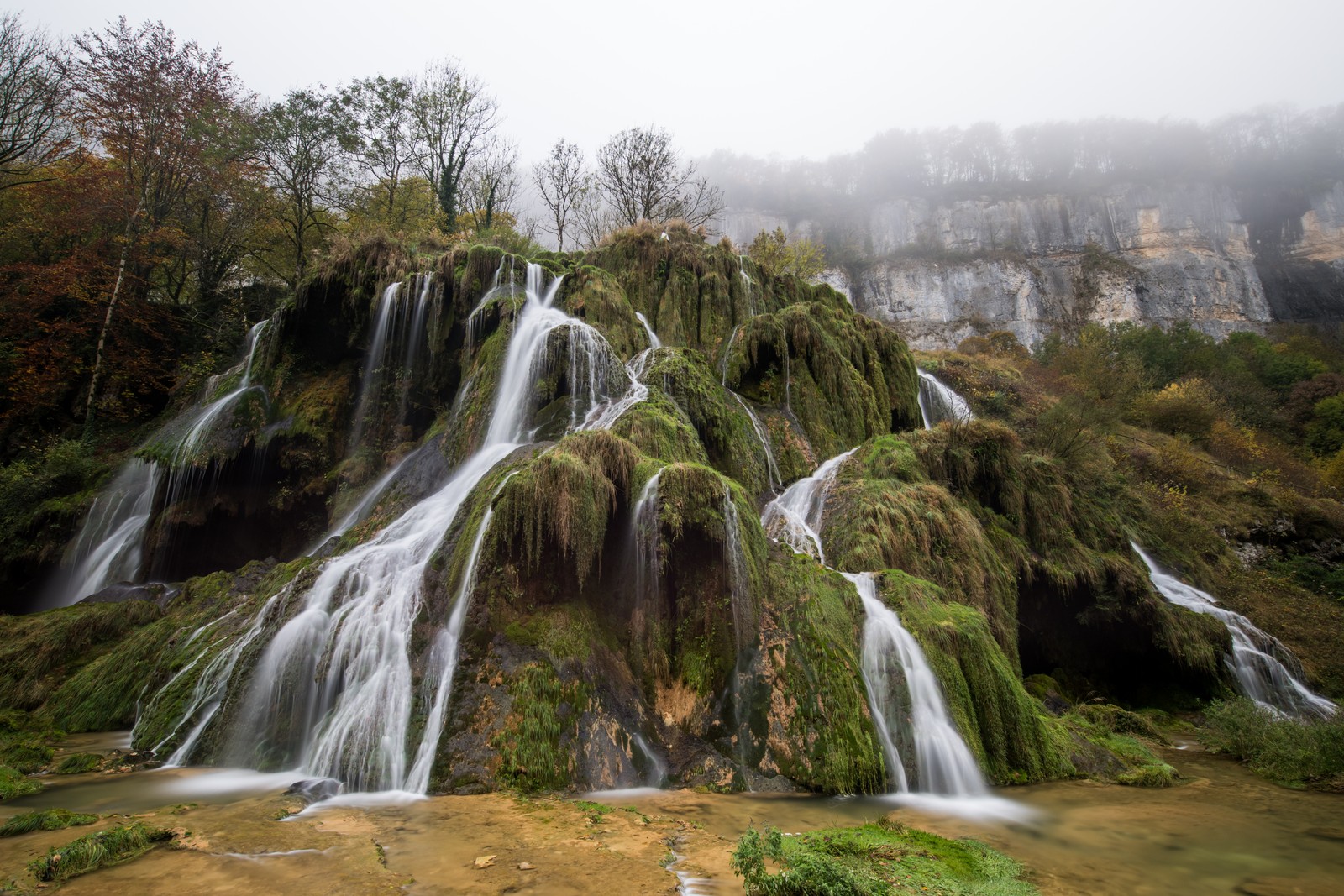 Uma cachoeira nas montanhas com algumas árvores no topo (cachoeira, reserva natural, natureza, recursos hídricos, corpo de água)