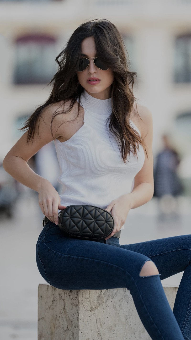 Femme arabe assise sur un pilier en pierre avec un sac noir (fille, chaud)