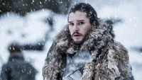 Jon Nieve en un paisaje nevado, vistiendo una capa de piel, con una expresión seria entre copos de nieve que caen.