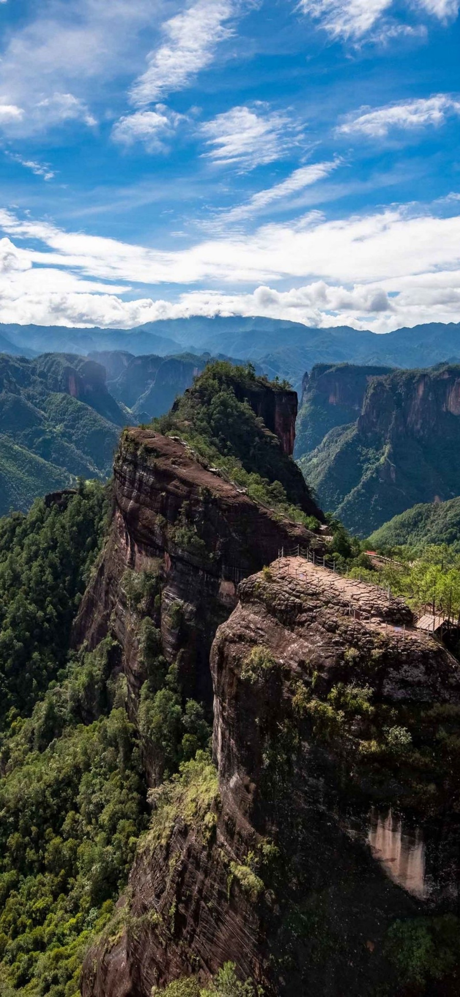 A view of a mountain with a cliff and a person standing on a ledge (highland, cloud, mountain, plant community, ecoregion)