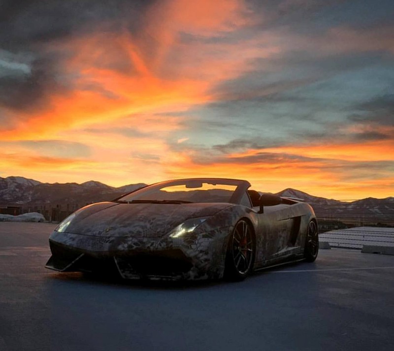 Un primer plano de un coche estacionado en una carretera con una puesta de sol de fondo (coche, fuego, lamborghini, cielo)