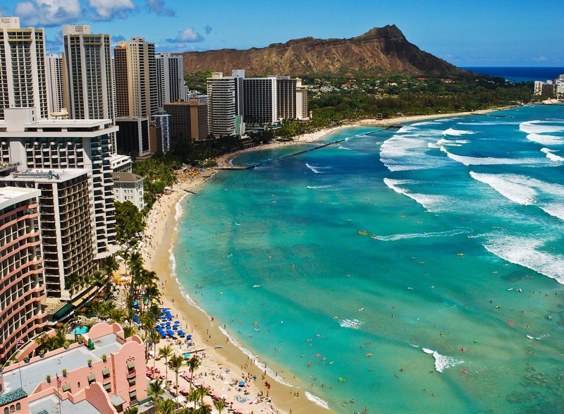 Uma vista aérea de uma praia com uma montanha ao fundo (aéreo, praia, edifícios, aproveitando, pessoas)