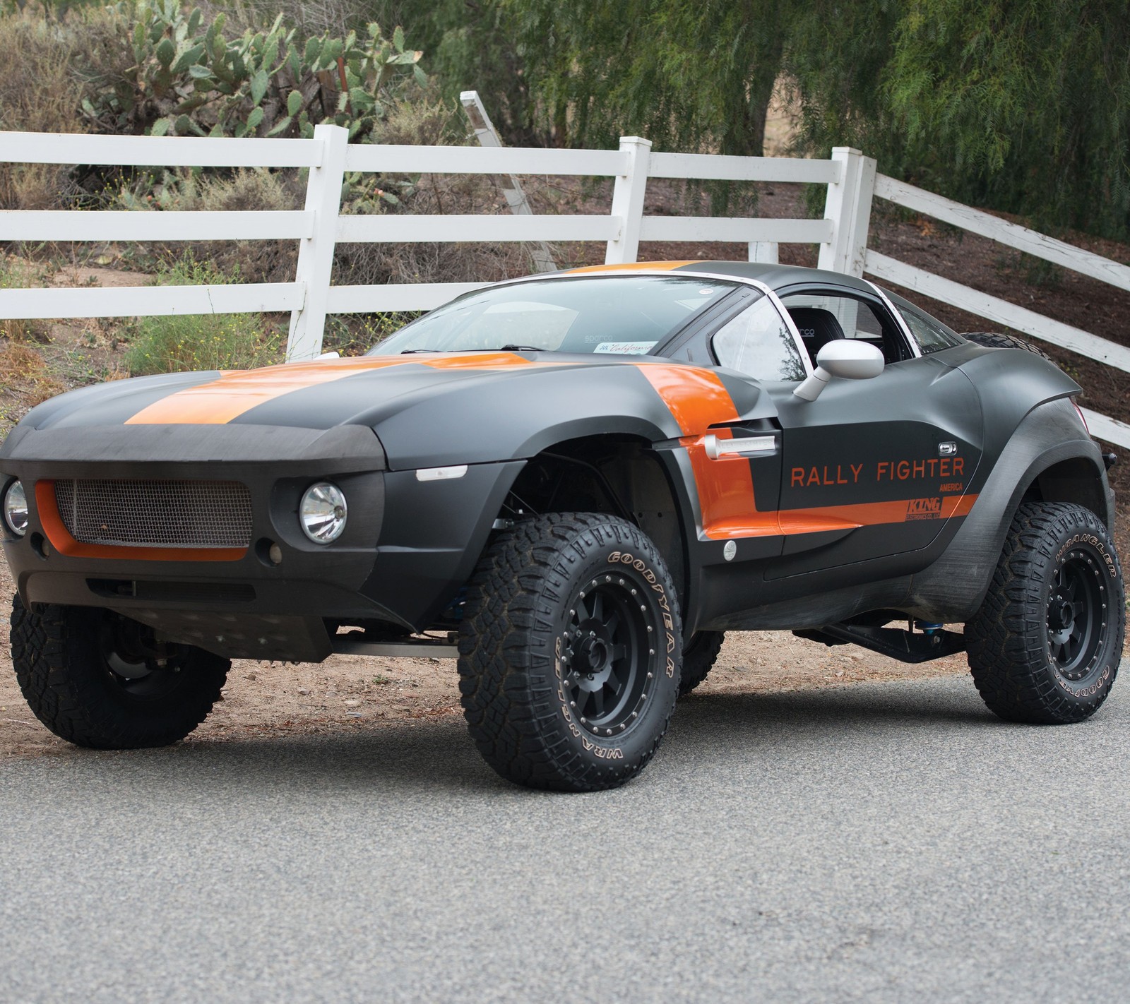 Véhicule avec des rayures orange garé sur une route près d'une clôture (combattant, tout terrain, orange, rallye)