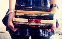 Stack of Diverse Books Held Against Tartan Fabric