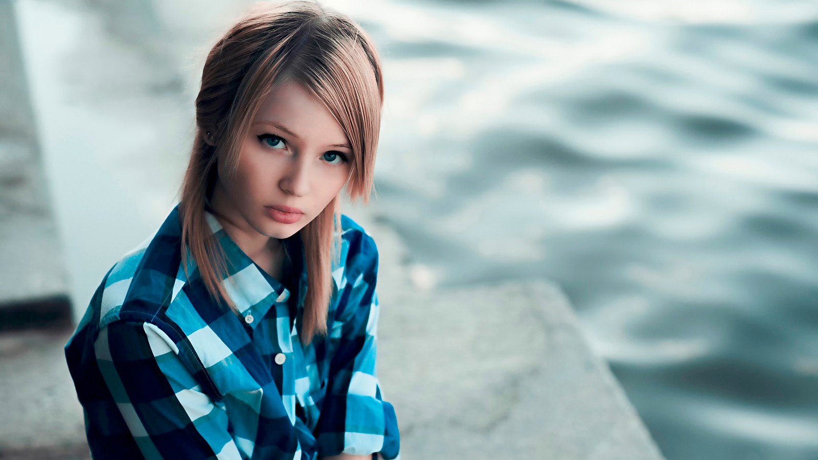 Une femme blonde aux yeux bleus assise sur un rebord près de l'eau (emily browning, modèle, bleu, beauté, cheveux longs)