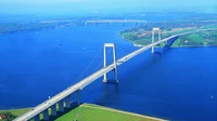 Aerial view of a cable-stayed bridge spanning a serene waterway, surrounded by lush greenery and a clear sky.