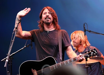 Dave Grohl se produisant en direct avec une guitare acoustique, engageant le public, tandis que le batteur est en arrière-plan.