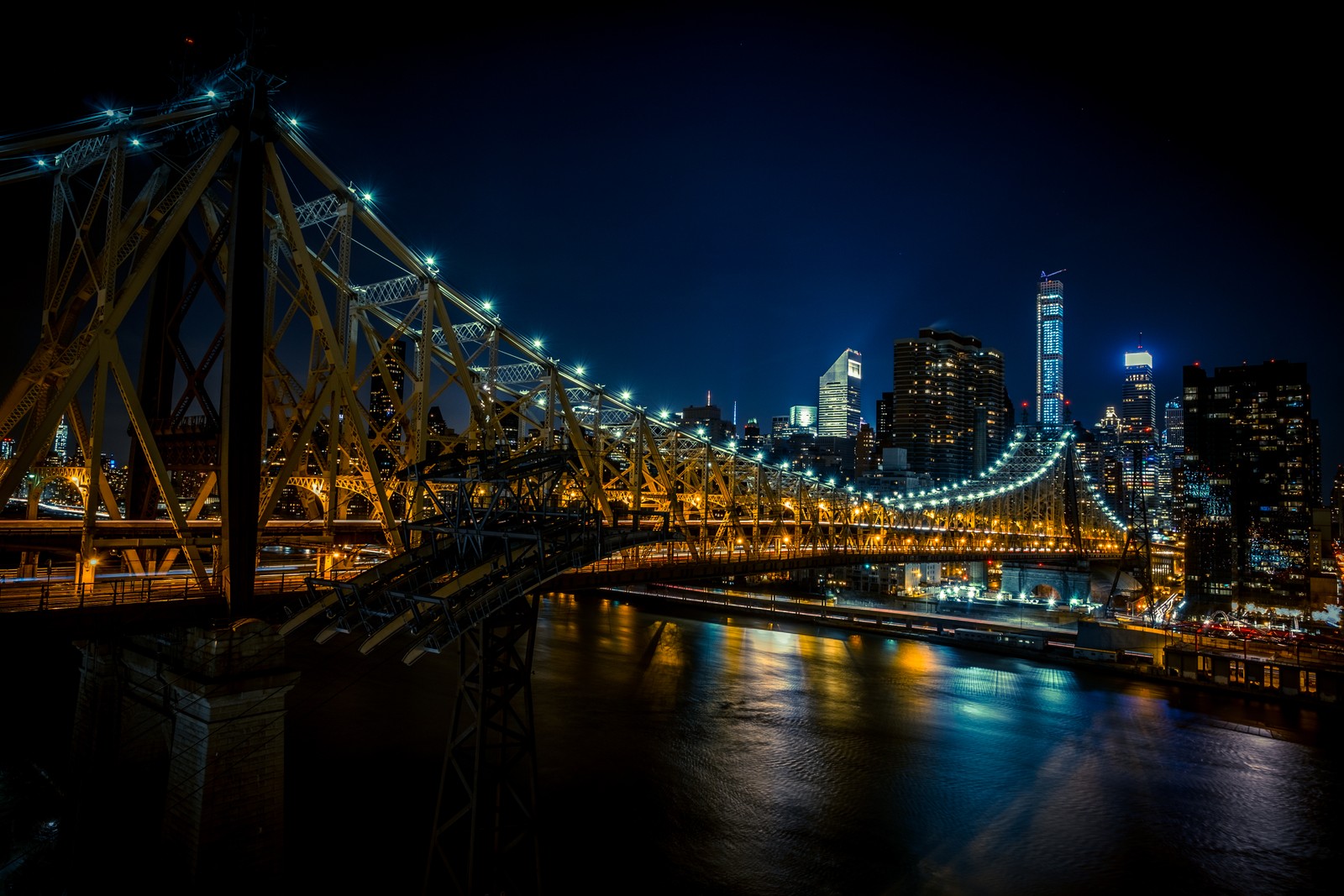 Una vista de un puente sobre un río con una ciudad de fondo (queensboro bridge, nueva york, new york city, puente voladizo, luces de la ciudad)