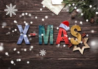 Colorful wooden letters spelling "X-MAS" adorned with a Santa Claus hat, surrounded by snowflakes, pine cones, and festive decorations on a rustic wooden background.