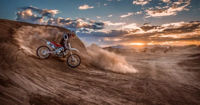 A motocross rider performs a dynamic turn on a sandy track at sunset, kicking up dust against a dramatic sky.